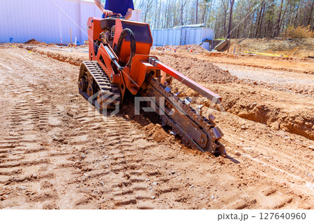 Heavy trenching machinery digs trench in soil for construction purposes on work site 127640960