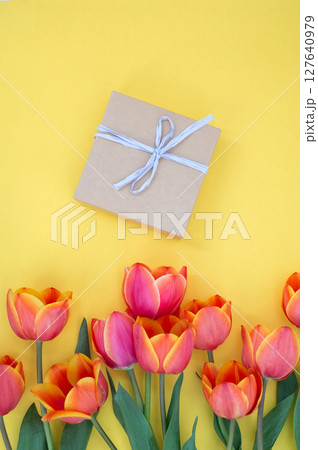 Gift box with white ribbon surrounded by vibrant tulips on yellow background Gift box with white ribbon surrounded by vibrant tulips on yellow background 127640979