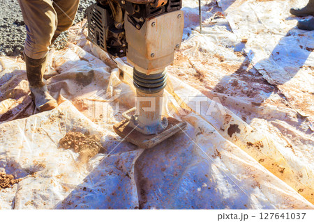 Construction worker uses tamper to compact soil on job site in preparate to foundation slab 127641037