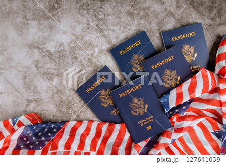 Five United States passports lie on gray surface beside American flag, symbolizing national identity. 127641039