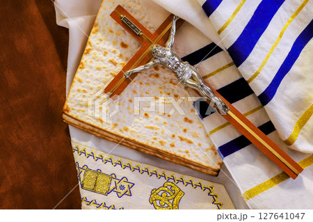 Crucifix on tallit prayer shawl traditional matzah religious symbols are arranged on table for Passover celebration. Crucifix on tallit prayer shawl traditional matzah religious symbols are arranged on table for Passover celebration. 127641047