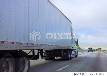 Large truck moves steadily along American highway with other vehicles in background under overcast skies. 127641087