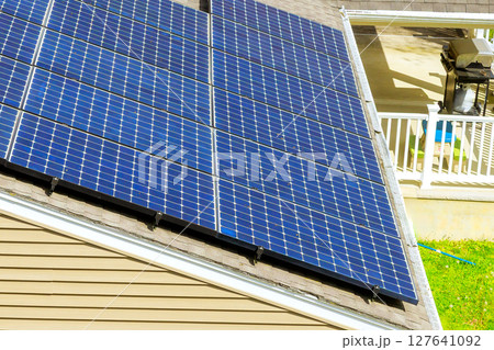 Several solar panels are mounted on sloped roof, capturing sunlight in quiet suburban area. 127641092