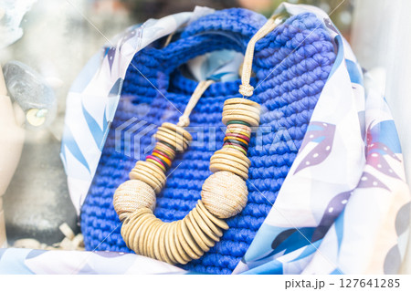 Colorful wooden necklace displayed on blue knitted bag. Handmade fashion, summer accessories, and artisan style in boutique showcase. 127641285