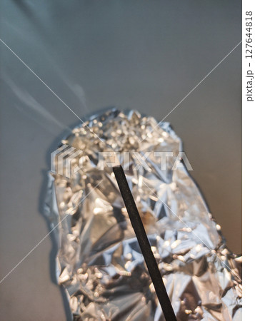 Incense stick burning on crumpled aluminum foil creating aromatic smoke copy space 127644818