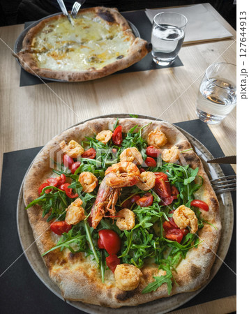 Gourmet pizza topped with succulent shrimp, peppery arugula, and sweet cherry tomatoes at rustic italian eatery in aosta 127644913