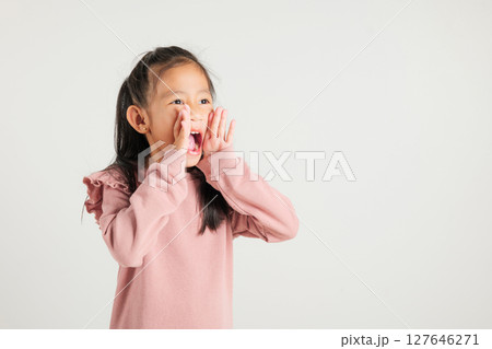 Asian happy portrait cute young kid girl standing hand on mouth talking news announcement studio shot isolated on white background, Thai kindergarten child announcement Asian happy portrait cute young kid girl standing hand on mouth talking news announcement studio shot isolated on white background, Thai kindergarten child announcement 127646271