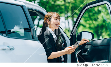 スマートフォンを持って車を降りる女性・ビジネスウーマン スマートフォンを持って車を降りる女性・ビジネスウーマン 127646699