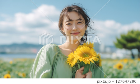 ライトグリーンのワンピースを着た女性がひまわりを抱えている 127647290