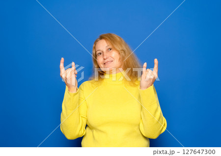 Delighted young ethnic female millennial with long dark hair in warm sweater and sunglasses, smiling brightly and showing rock gesture while listening to favorite song against yellow background Delighted young ethnic female millennial with long dark hair in warm sweater and sunglasses, smiling brightly and showing rock gesture while listening to favorite song against yellow background 127647300