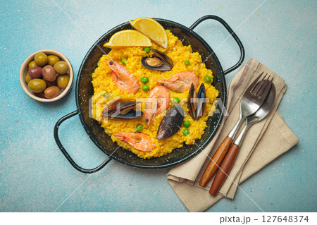 Spanish seafood Paella with shrimps, mussels, peas and lemon in a pan on light blue background top view. Mediterranean meal Spanish seafood Paella with shrimps, mussels, peas and lemon in a pan on light blue background top view. Mediterranean meal 127648374