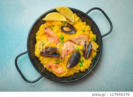 Spanish seafood Paella with shrimps, mussels, peas and lemon in a pan on light blue background top view. Mediterranean meal 127648376