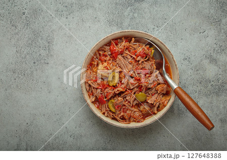Ropa vieja with white rice, tomato sauce and green olives on a plate top view, traditional dish of Cuba, space for text 127648388