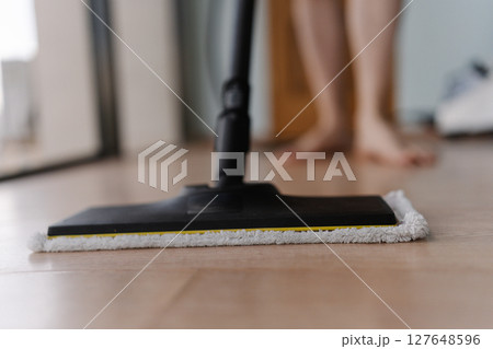 Cropped shot of unrecognizable man washing hardwood floor with steam cleaner mop in modern apartment, ensuring hygiene and cleanliness, close-up. Concept of modern housekeeping appliance. 127648596