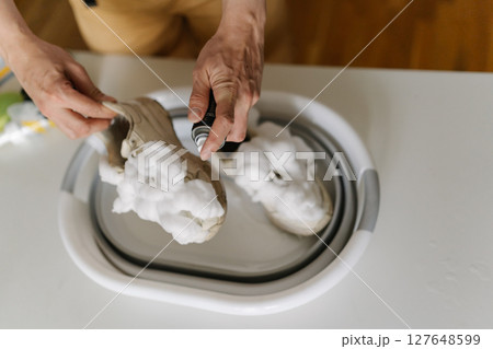 Cleaning white sneakers with foam spray, male hands washing athletic shoes in bathroom sink, focusing on footwear hygiene and thorough maintenance, closeup. Concept of maintaining hygiene, cleanliness Cleaning white sneakers with foam spray, male hands washing athletic shoes in bathroom sink, focusing on footwear hygiene and thorough maintenance, closeup. Concept of maintaining hygiene, cleanliness 127648599