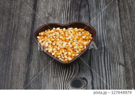 Unpopped popcorn in a wooden bowl on wooden background. A type of corn that expands from the kernel and puffs up when heated. Yellow seeds, edible, raw and vegan food. Isolated macro photo close up. Unpopped popcorn in a wooden bowl on wooden background. A type of corn that expands from the kernel and puffs up when heated. Yellow seeds, edible, raw and vegan food. Isolated macro photo close up. 127648979