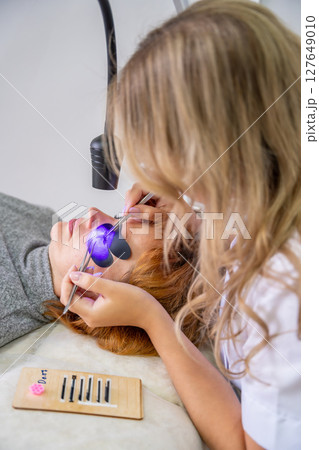 Eyelash extension procedure using ultraviolet lamp in modern beauty salon. Innovative lash enhancement technology with precise application technique. 127649010