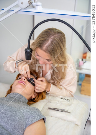 Beautician applying black eye patches before eyelash extension procedure with ultraviolet lamp. Innovative lash extension method in modern beauty salon 127649013