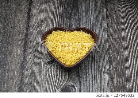 White gluten free vermicelli made from rice flour. Italian pasta in wooden spoon on dark textured background. Top view, space for text. 127649032