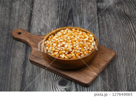 Unpopped popcorn in a wooden bowl on wooden background. A type of corn that expands from the kernel and puffs up when heated. Yellow seeds, edible, raw and vegan food. Isolated macro photo close up. 127649065