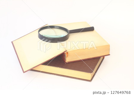 Still life from a magnifier and a pile of old books on a white background 127649768