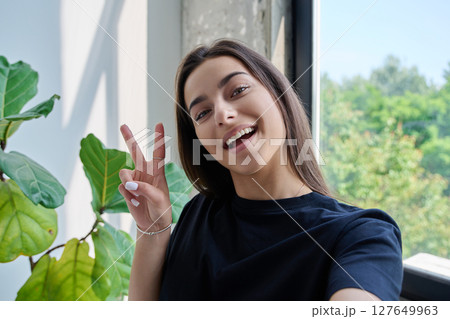 Close-up selfie portrait of teenage female looking at web camera showing victory gesture Close-up selfie portrait of teenage female looking at web camera showing victory gesture 127649963