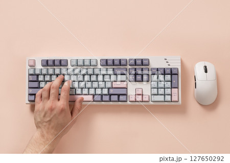 Mans hand texting and typing on modern mechanical keyboard and mouse on pink desk as background. Colorful pink and gray key cap. View from above. Flat lay. 127650292