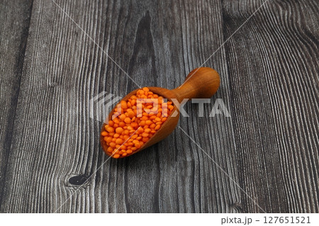 Red lentils in wooden scoop, isolated on wooden background. 127651521
