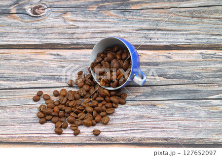 Close-up and top view of hot black coffee in blue coffee cup and roasted Thai coffee beans on wooden background. 127652097