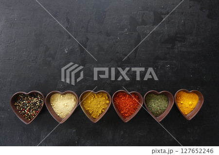 Different kind of spices on a black stone. Oriental spices in in heart shaped bowl, 127652246