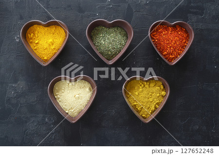 Different kind of spices on a black stone. Oriental spices in in heart shaped bowl, 127652248