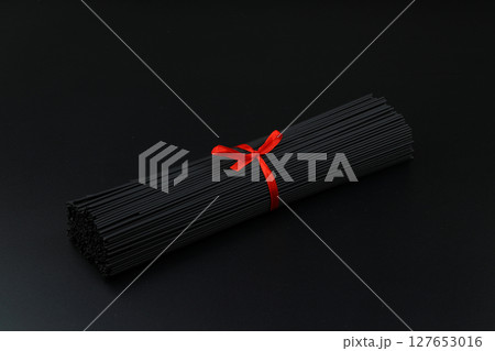 Raw black homemade spaghetti bunch isolated. Dry black noodles macaroni bundle. Close-up 127653016