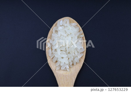 White uncooked rice in wooden spoons on black background. Raw grains of long rice are scattered on table. Natural organic vegan food. Traditional Asian cereal culture. 127653229