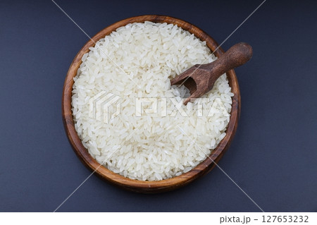 Raw white rice on black background. Long uncooked rice in wooden plate. Natural organic food. Traditional Asian cereal culture. Raw white rice on black background. Long uncooked rice in wooden plate. Natural organic food. Traditional Asian cereal culture. 127653232
