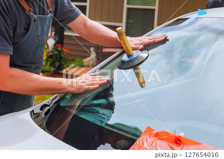 Technician uses suction cup tool to secure new windshield in car at home driveway 127654010