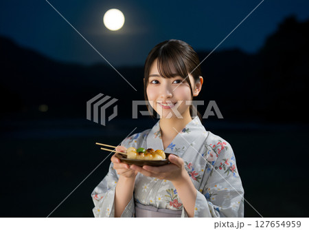 満月の夜に和装姿で団子を持つ日本人女性の風情あるポートレート 127654959