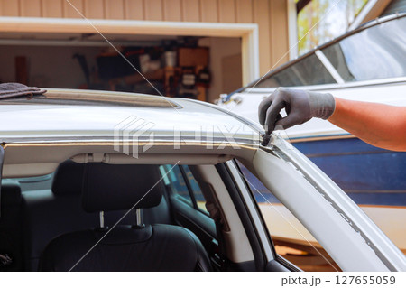 Worker works on sealing window trim of car in garage filled with car maintenance tools. 127655059
