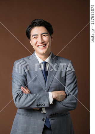 茶色背景でスーツを着た腕を組む悩む考えるビジネスマンの社長のイメージ 笑顔 茶色背景でスーツを着た腕を組む悩む考えるビジネスマンの社長のイメージ 笑顔 127655873