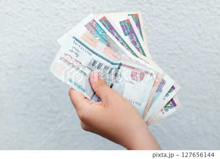 counting Egyptian pound banknotes against a white wall 127656144