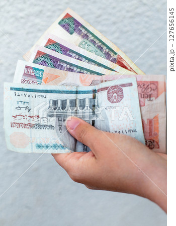 counting Egyptian pound banknotes against a white wall 127656145