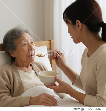 ベッド横で家族が介助（食事・手を握る・声かけ） 127656820