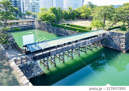 香川県、史跡高松城跡玉藻公園のお堀に掛かる鞘橋と琴電の高松築港駅 127657895