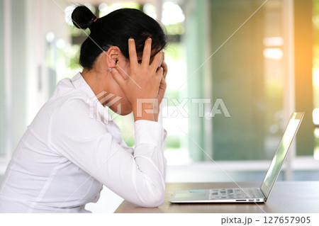 woman sitting down, his face unsettled. At the computer desk she has headaches and stress. Cause of hard work and insufficient rest. 127657905