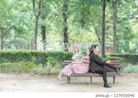 森の中のベンチに座ってピンクのドレスでウェディングフォトを撮るカップル 森の中のベンチに座ってピンクのドレスでウェディングフォトを撮るカップル 127658040