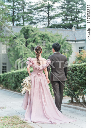 洋館の庭をピンクのドレスで歩きウェディングフォトを撮るカップル 127658231