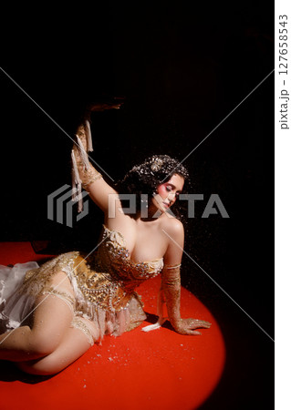 Woman in vintage corset lying on red stage floor under hanging beads on dark background Woman in vintage corset lying on red stage floor under hanging beads on dark background 127658543