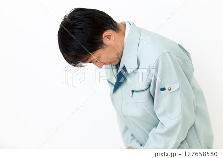 グリーンの作業服を着て謝罪をするミドル男性ビジネスマン グリーンの作業服を着て謝罪をするミドル男性ビジネスマン 127658580