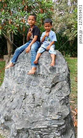 two boys sitting on a big rock 127659431
