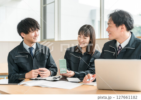 ビルの模型を見ながら会議,ミーティングする作業着姿の男女のビジネスマン ビルの模型を見ながら会議,ミーティングする作業着姿の男女のビジネスマン 127661182