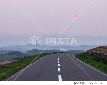 北海道美瑛町の丘の上の道の向こうに夕日が沈む風景 北海道美瑛町の丘の上の道の向こうに夕日が沈む風景 127661376